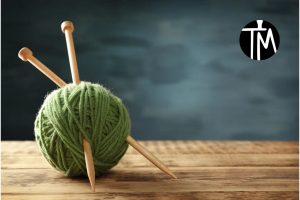 Ein Wollknäuel mit zwei Stricknadeln. Oben rechts das TM-logo für Tante Martin
